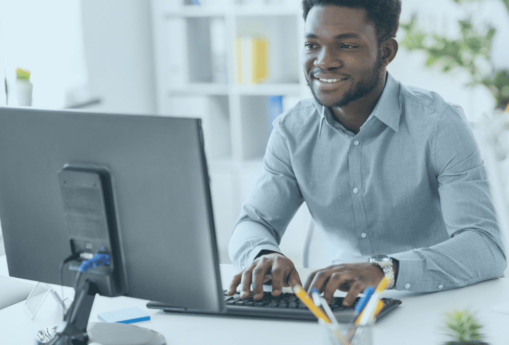 Young male smiling business administrator sitting at a desk in front of a computer screen