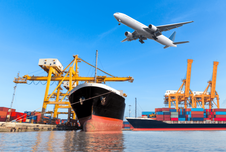 a big cargo ship in a port in front of cranes and an aeroplane in the air flying above it