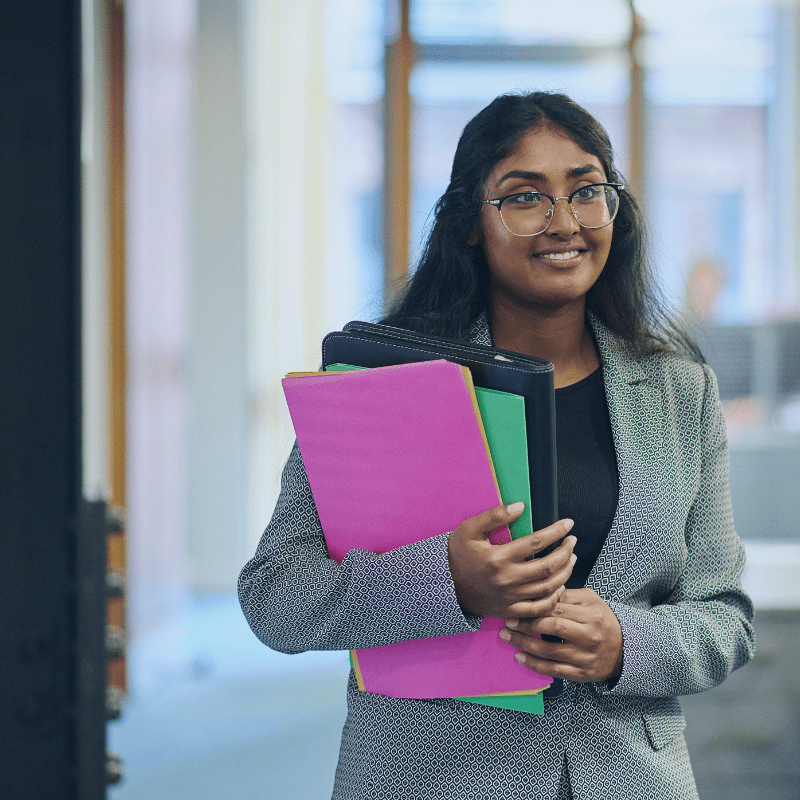 young female office worker standing and smiling whilst holding some paperwork in an office setting