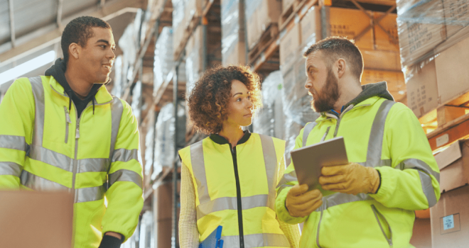 A woman and two men in hi-vis jackets inside a warehouse