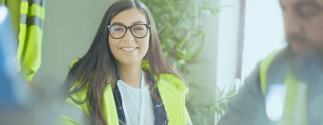Young woman with long hair and glasses and hi-vis vest smiling at camera